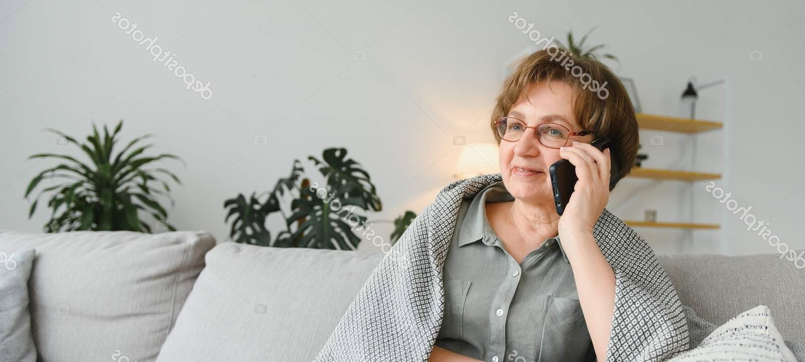 beautiful senior woman in casual clothing using her smart phone while sitting on the sofa at home